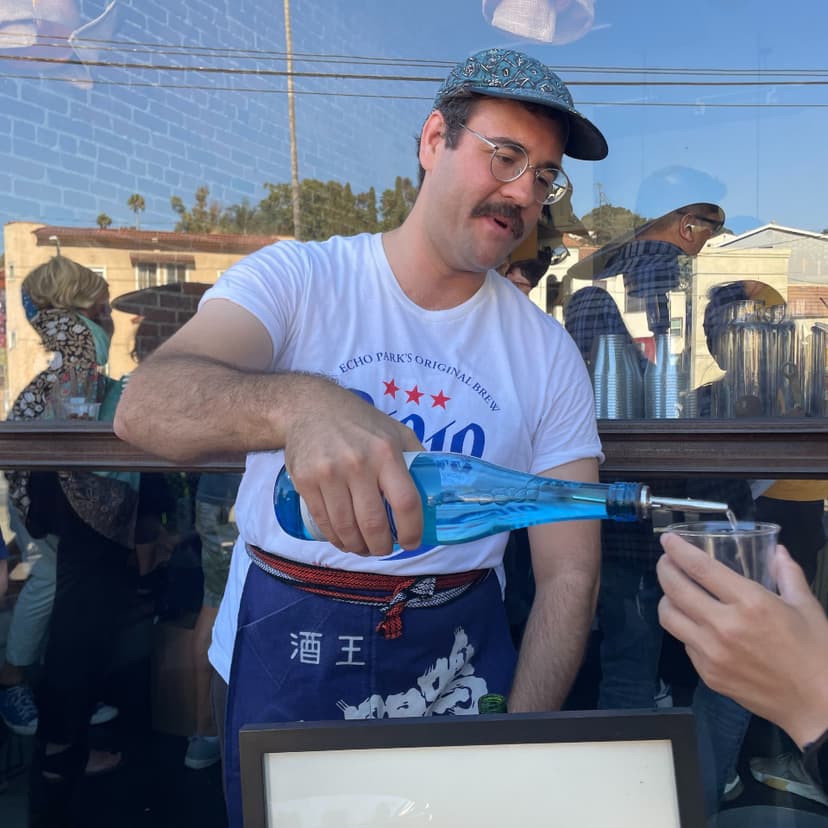 Photo of me pouring sake from a blue bottle in front of a glass window.